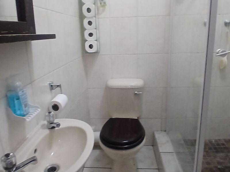 A functional bathroom featuring a pedestal basin, toilet, and a glass-enclosed shower with tiled finishes throughout.