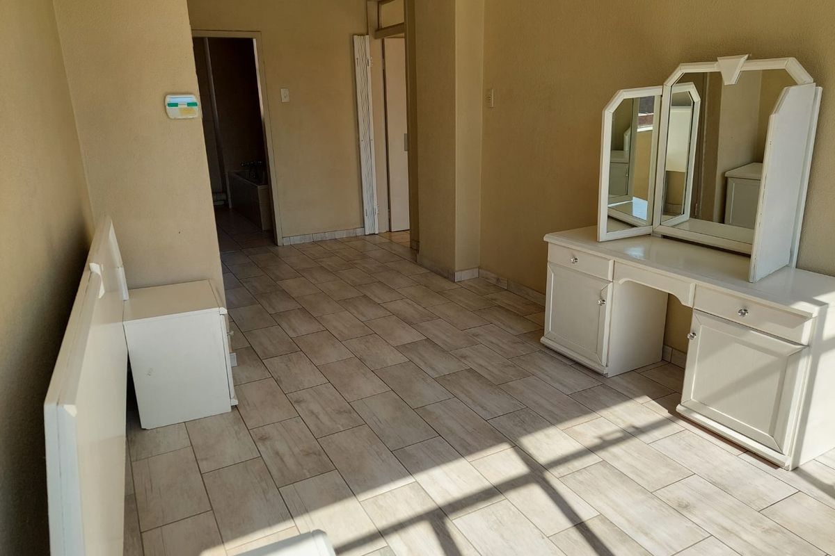 A bedroom featuring light-toned tiled flooring and neutral wall finishes, with direct access to an adjoining bathroom area.