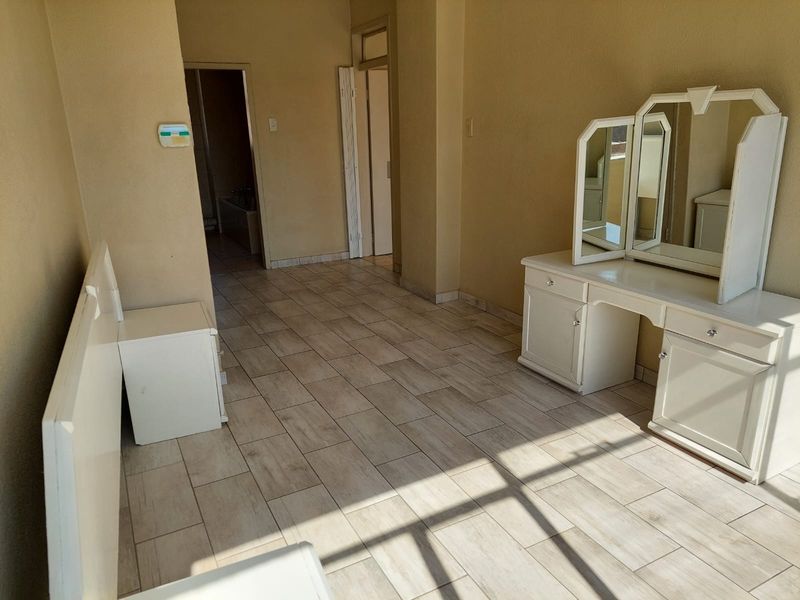 A bedroom featuring light-toned tiled flooring and neutral wall finishes, with direct access to an adjoining bathroom area.