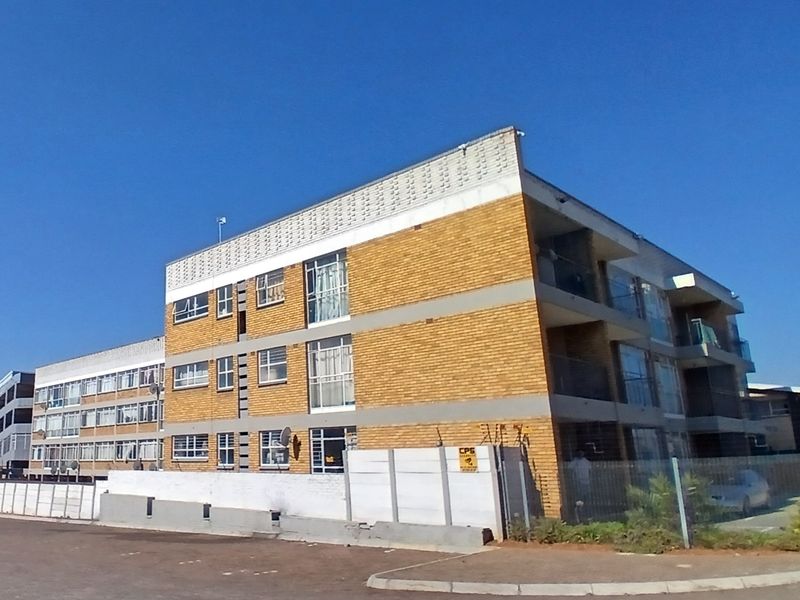 Exterior view of a multi-story apartment building featuring a brick facade, private balconies, and secure perimeter fencing.