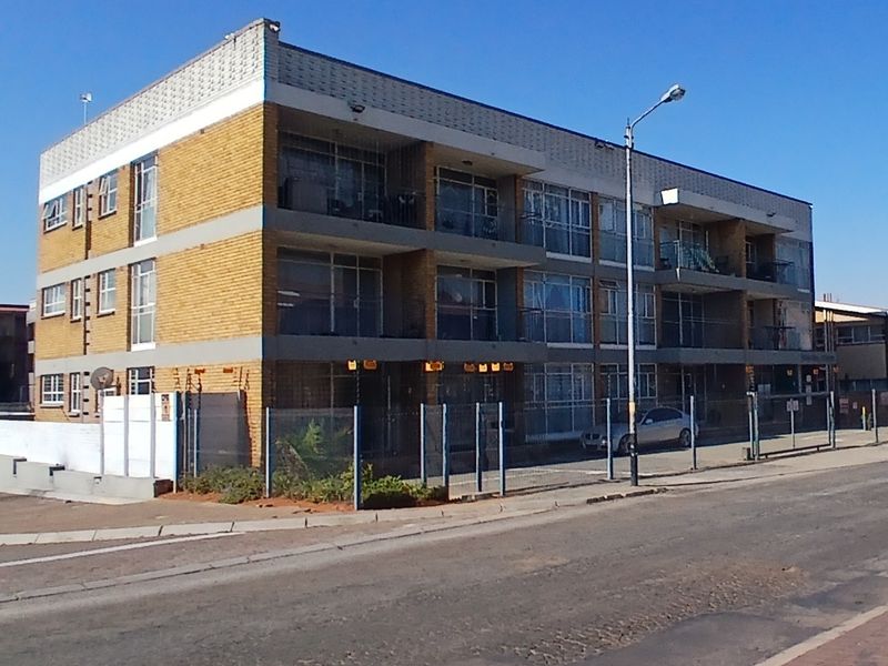 A multi-story apartment building featuring brick facade, private balconies, and secure perimeter fencing along the street front.