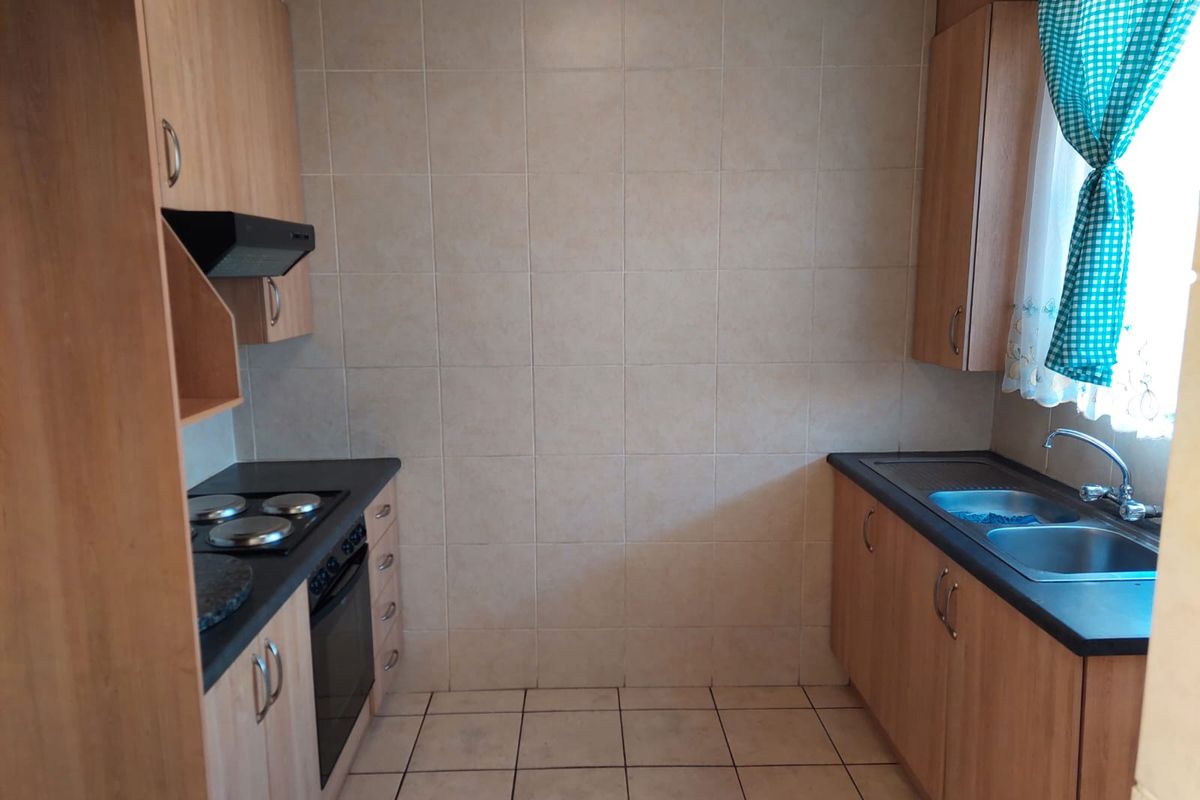 Functional kitchen featuring laminate cabinetry, built-in oven with electric hob, extractor fan, and a double bowl stainless steel sink with tiled splashback.