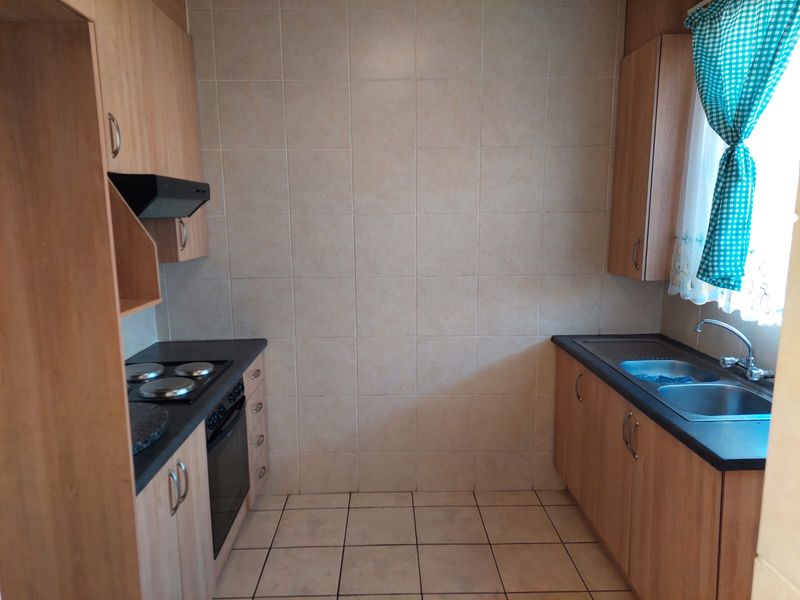 Functional kitchen featuring laminate cabinetry, built-in oven with electric hob, extractor fan, and a double bowl stainless steel sink with tiled splashback.