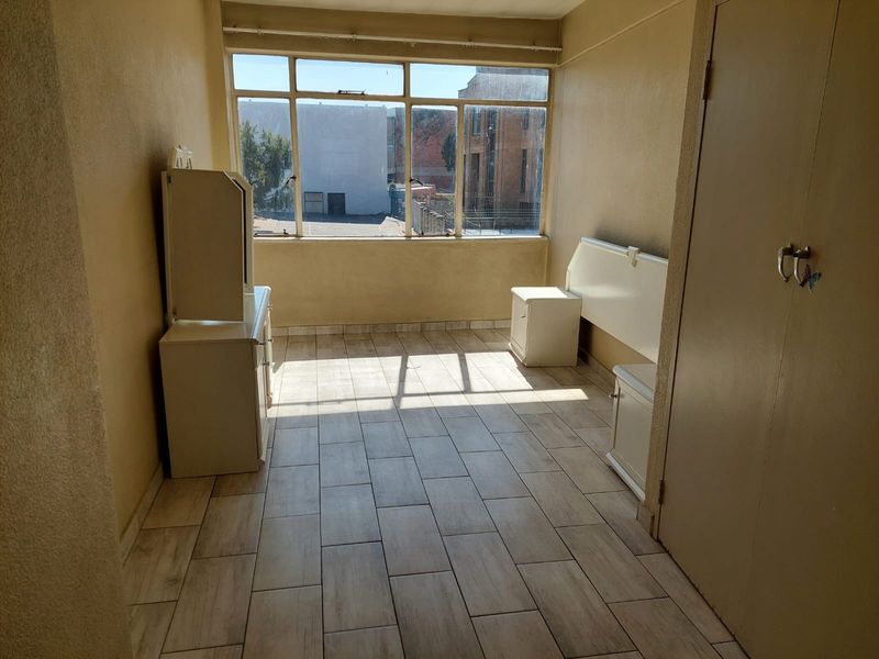 A bright, empty bedroom featuring tiled flooring, a large window providing natural light, and a built-in cupboard, ready for personalization.