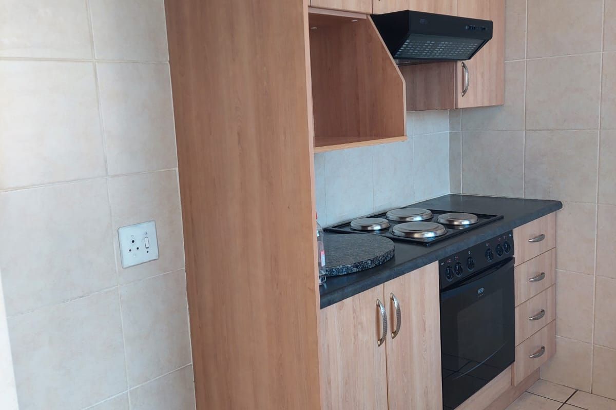 A functional kitchen featuring light wood-finish cabinetry, built-in oven and hob, extractor fan, and neutral tiled flooring and splashbacks.