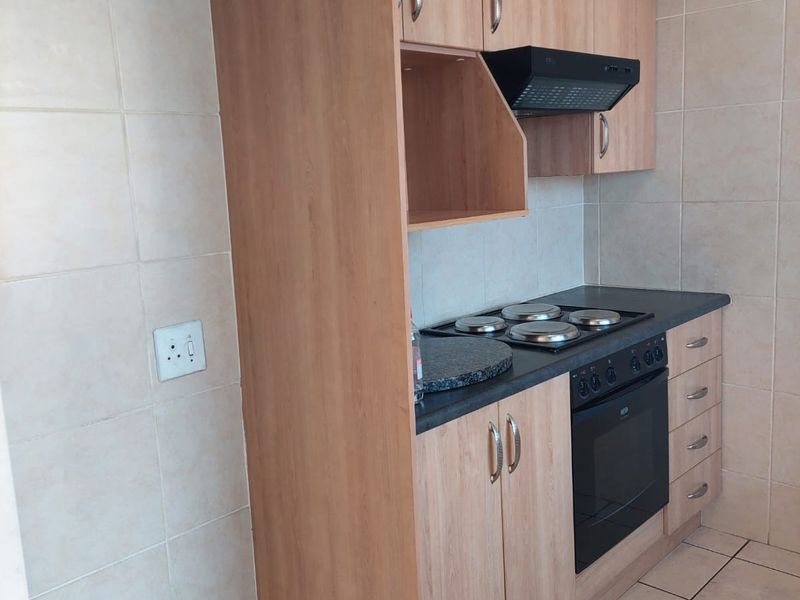 A functional kitchen featuring light wood-finish cabinetry, built-in oven and hob, extractor fan, and neutral tiled flooring and splashbacks.