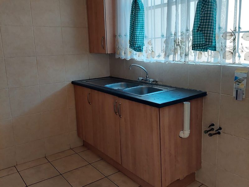 A functional kitchen area featuring tiled flooring, a double sink with laminate cabinetry, and tiled splashbacks, ready for modernization.
