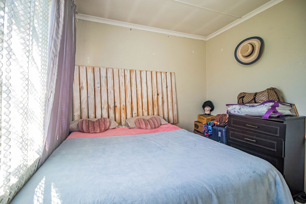 A compact bedroom featuring neutral wall tones and a window with curtains, requiring minor cosmetic updates to improve its overall appeal.