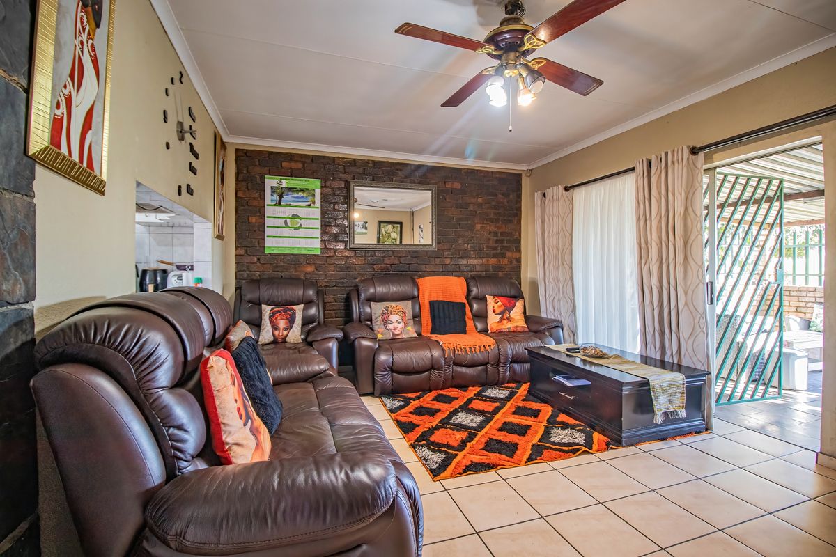 A comfortable living room featuring an exposed brick accent wall, tiled flooring, and a ceiling fan, with direct access to an outdoor patio area.