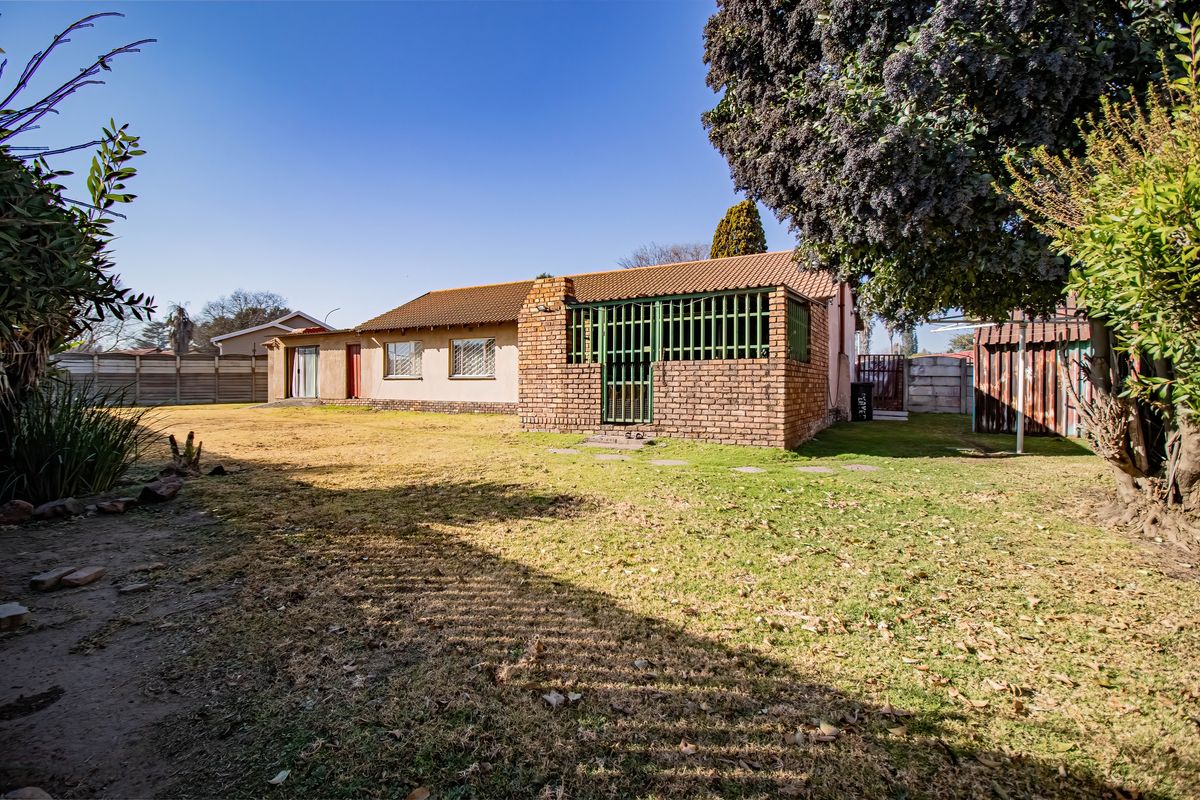 Rear view of the property featuring a brick facade, tiled roof, and a spacious backyard with established lawn and security features.