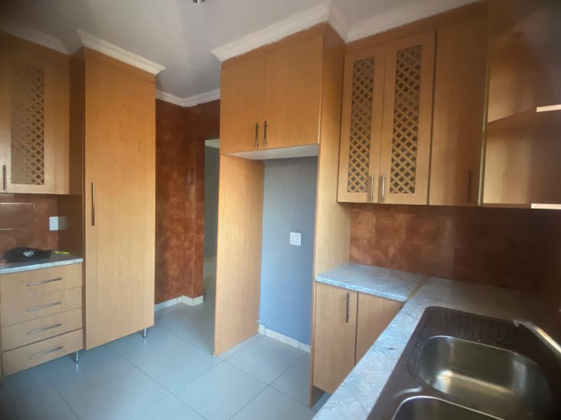 A functional kitchen featuring light wood-toned built-in cabinetry, double bowl sink, laminate countertops, and tiled flooring, offering a clean and practical workspace.