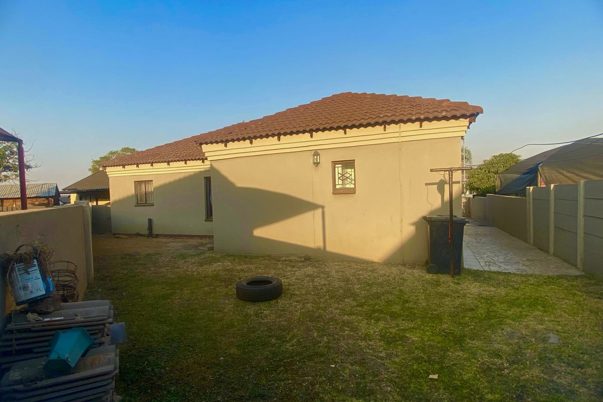 Rear view of the property featuring a tiled roof, plastered exterior walls, and a private garden area with a paved side walkway.