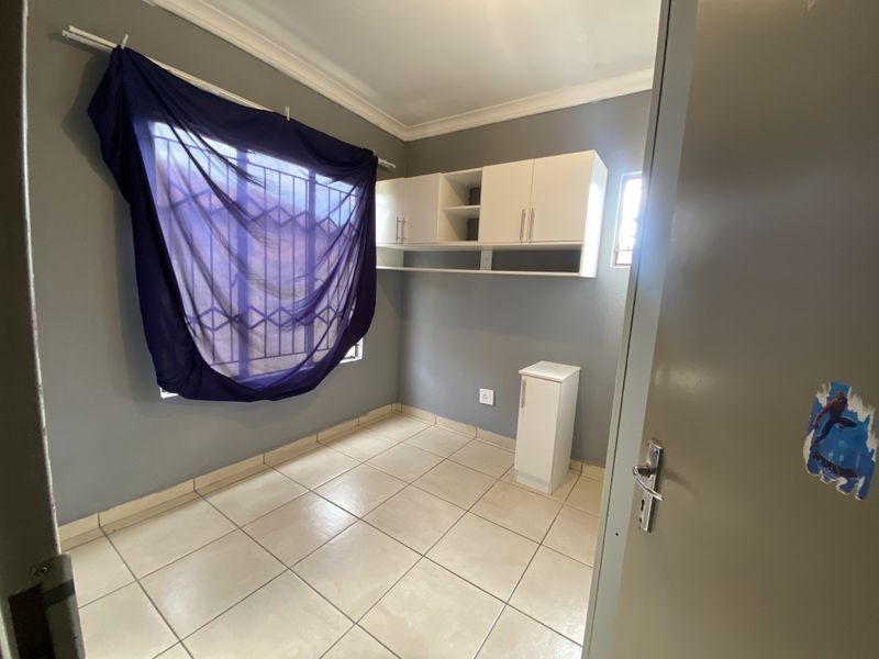 A compact bedroom featuring tiled flooring, built-in wall-mounted cabinetry, and security bars on the window.