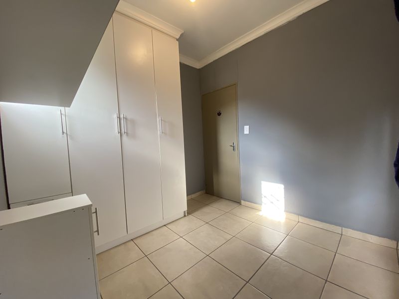 A clean, empty bedroom featuring neutral tiled flooring, built-in white cupboards, and grey painted walls, offering a versatile space ready for personalization.