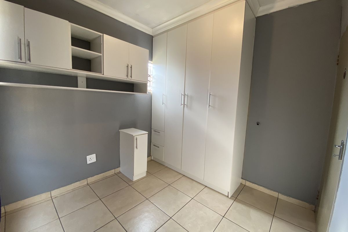 A clean, empty bedroom featuring neutral grey walls, tiled flooring, and ample built-in cupboard storage with additional wall-mounted shelving units.