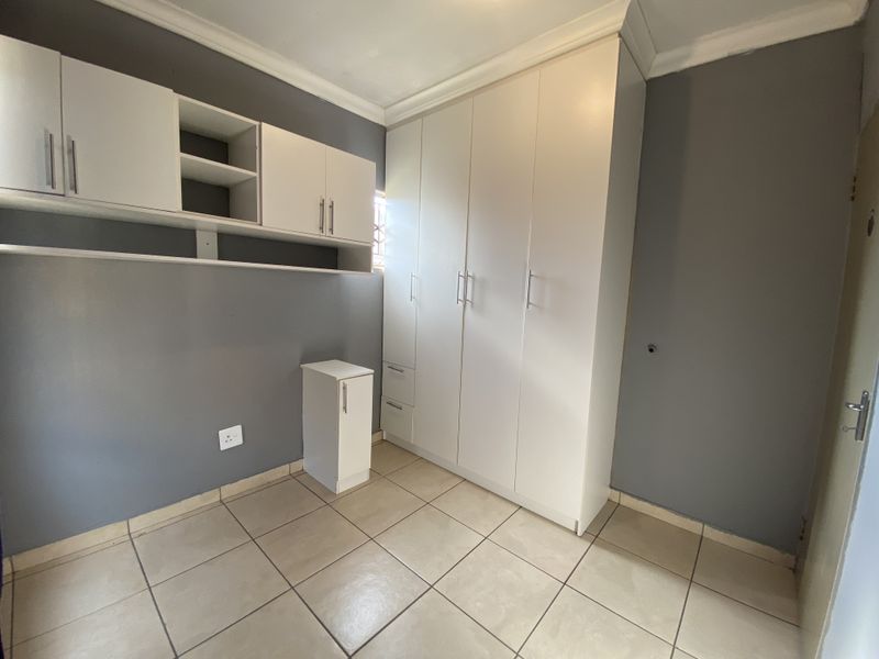 A clean, empty bedroom featuring neutral grey walls, tiled flooring, and ample built-in cupboard storage with additional wall-mounted shelving units.