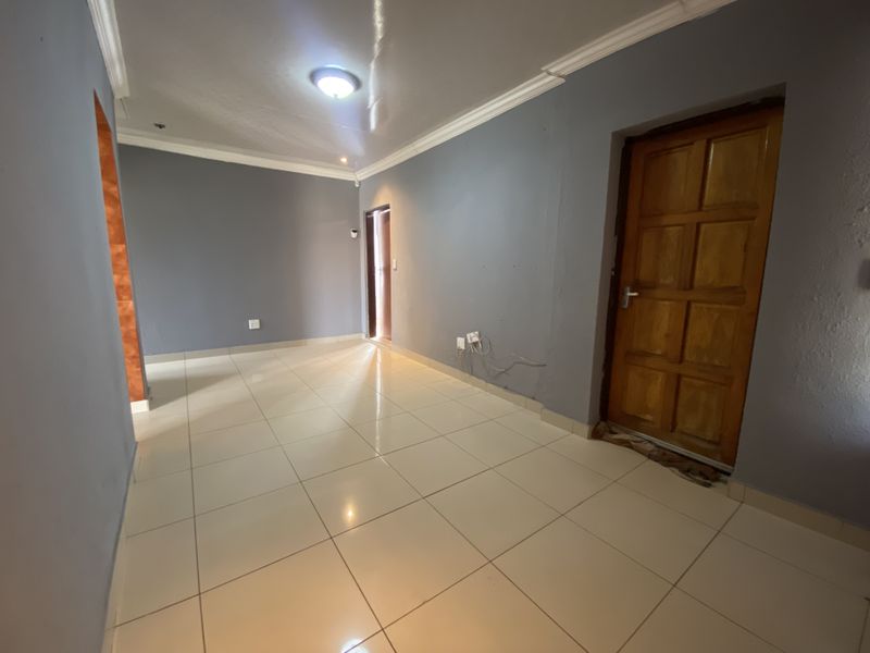 An empty living area featuring tiled flooring, grey painted walls, and a timber panel door, providing a blank canvas for interior design.