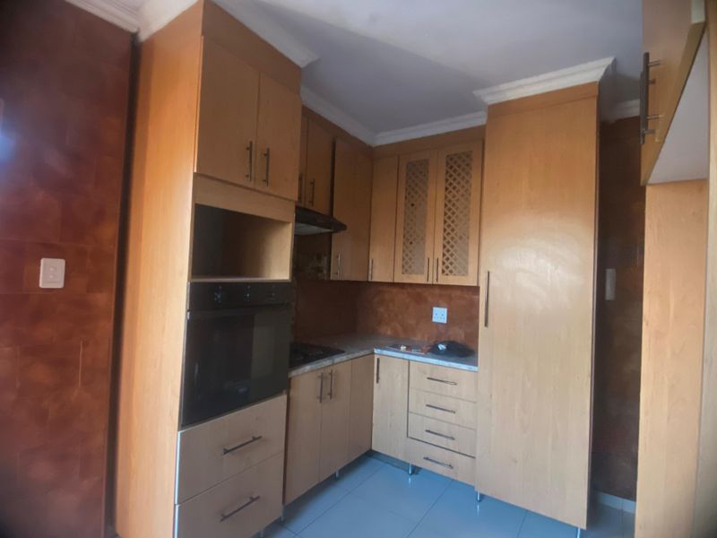 A functional kitchen featuring light wood cabinetry, built-in oven, extractor fan, and tiled flooring, offering a clean and practical workspace.