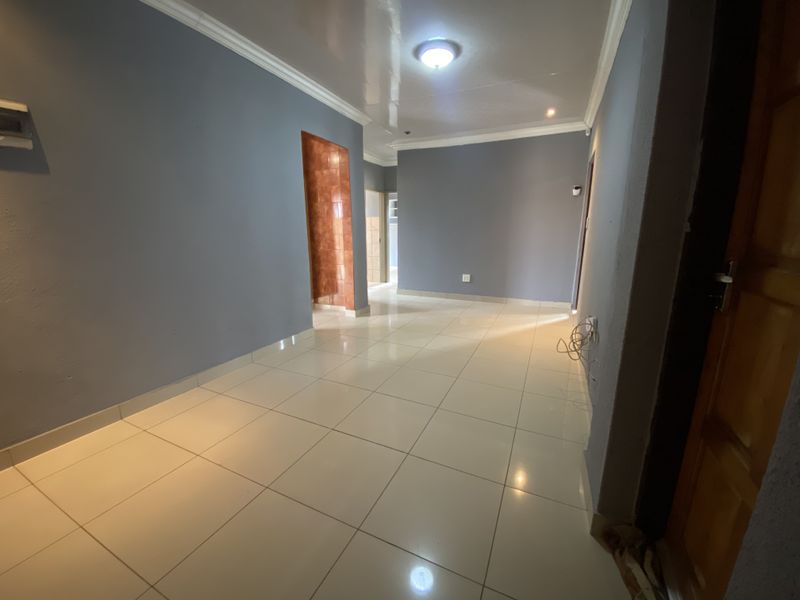An empty living area featuring neutral grey walls, polished floor tiles, and coved ceiling detailing, providing a blank canvas for interior design.
