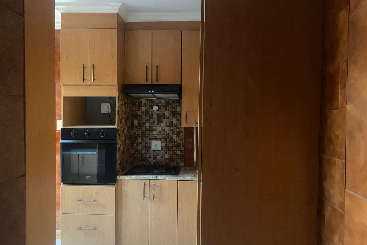 Compact kitchen featuring light wood-finish cabinetry, built-in oven, hob, extractor fan, and a decorative mosaic tile backsplash.
