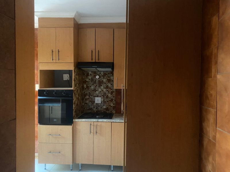 Compact kitchen featuring light wood-finish cabinetry, built-in oven, hob, extractor fan, and a decorative mosaic tile backsplash.