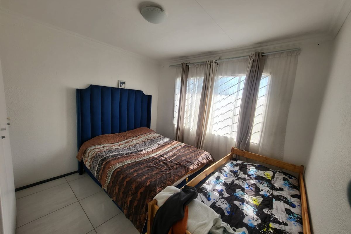A functional bedroom featuring tiled flooring, large windows with security bars, and neutral wall finishes, providing a practical space for rest.