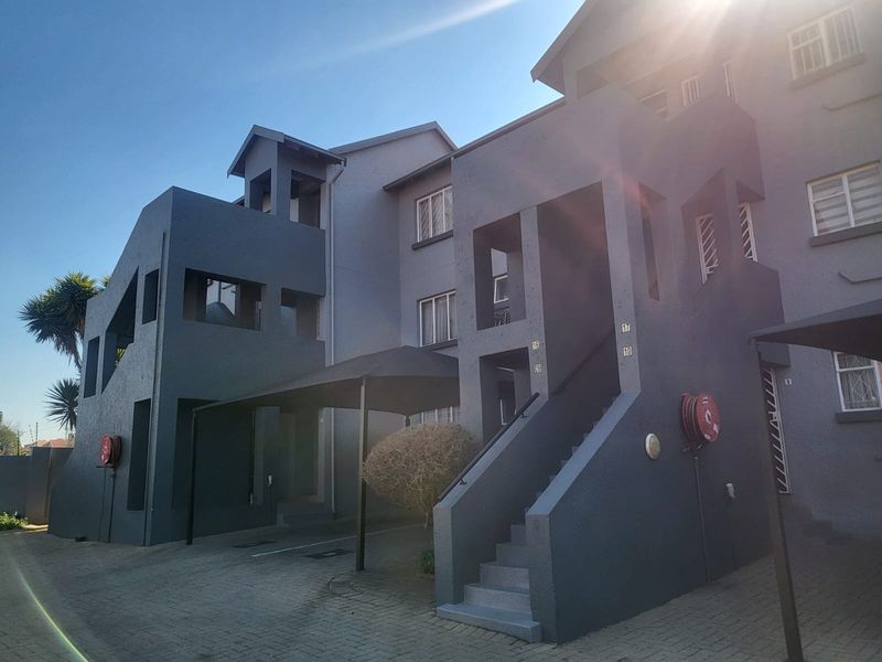 Front exterior view of a multi-story townhouse complex featuring paved driveway, covered parking, and external staircases with security features.