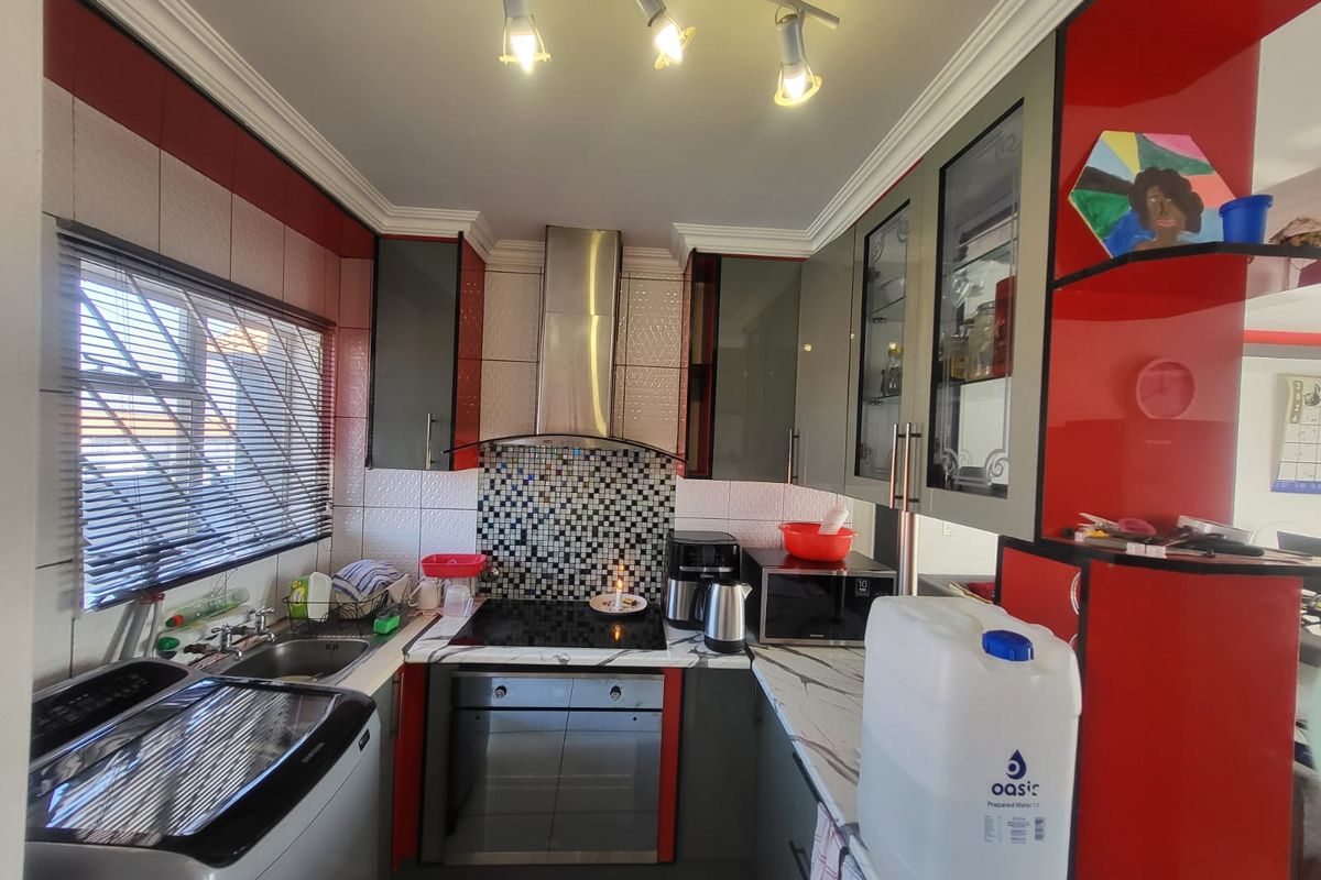 A compact kitchen featuring modern grey and red cabinetry, a mosaic tile backsplash, built-in oven and hob, and marble-look countertops.