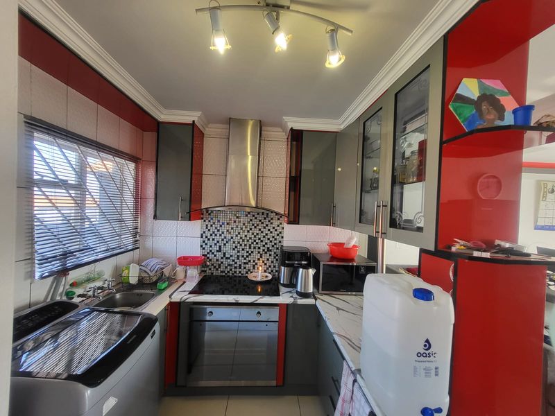 A compact kitchen featuring modern grey and red cabinetry, a mosaic tile backsplash, built-in oven and hob, and marble-look countertops.