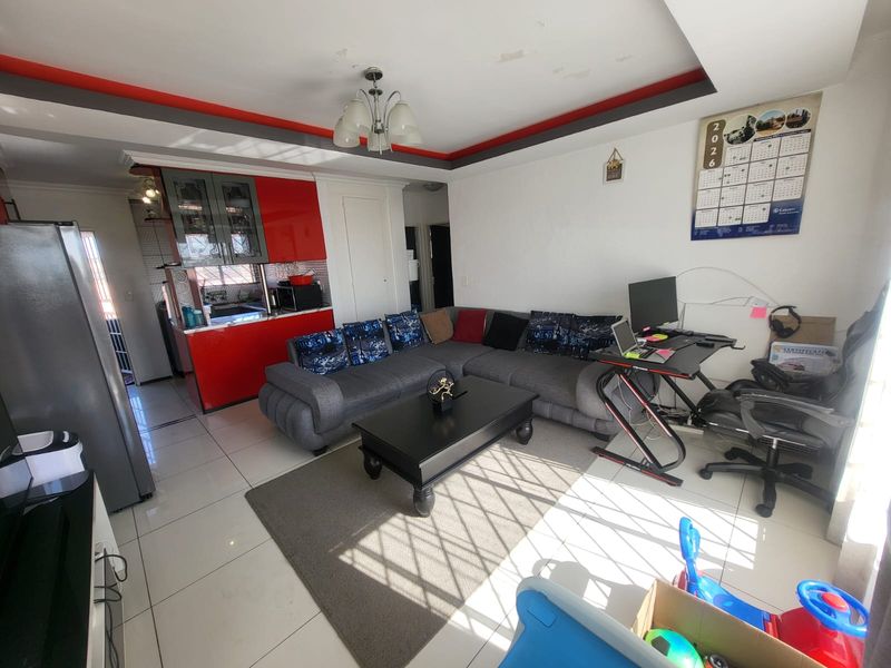 Open-plan living area featuring tiled floors and a vibrant red kitchen with glossy cabinetry, offering a functional layout for modern living.