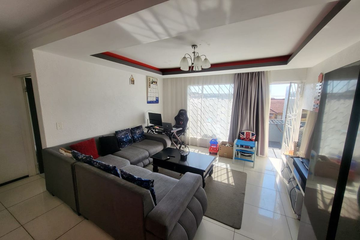 A living room featuring tiled flooring, a recessed ceiling design, and a sliding door leading to an outdoor area with security gates.