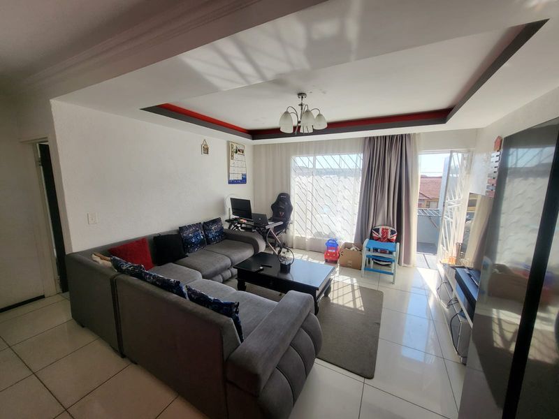 A living room featuring tiled flooring, a recessed ceiling design, and a sliding door leading to an outdoor area with security gates.