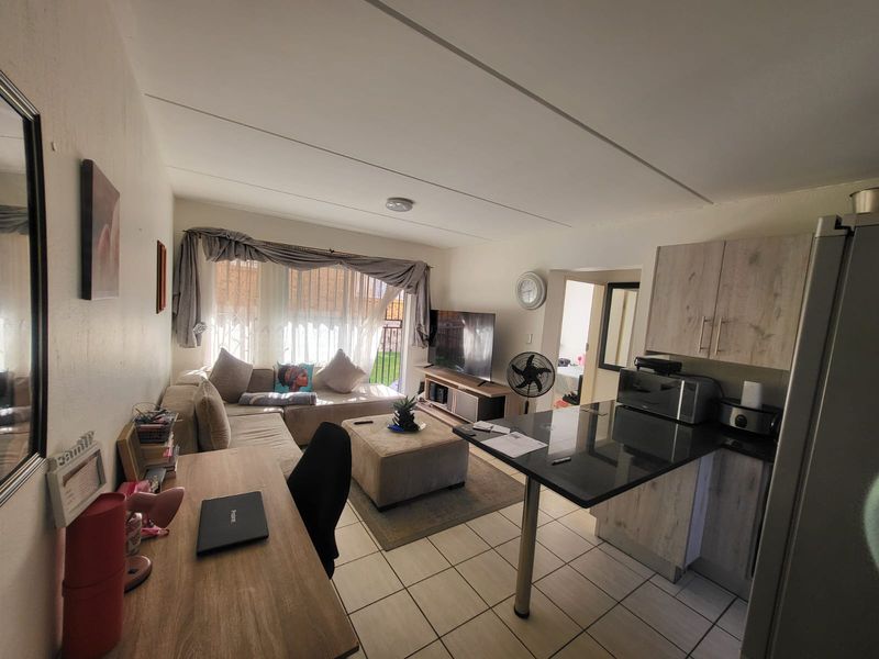 Open-plan living area featuring tiled floors, a compact kitchen with granite countertops, and a breakfast bar, leading to an outdoor patio area.