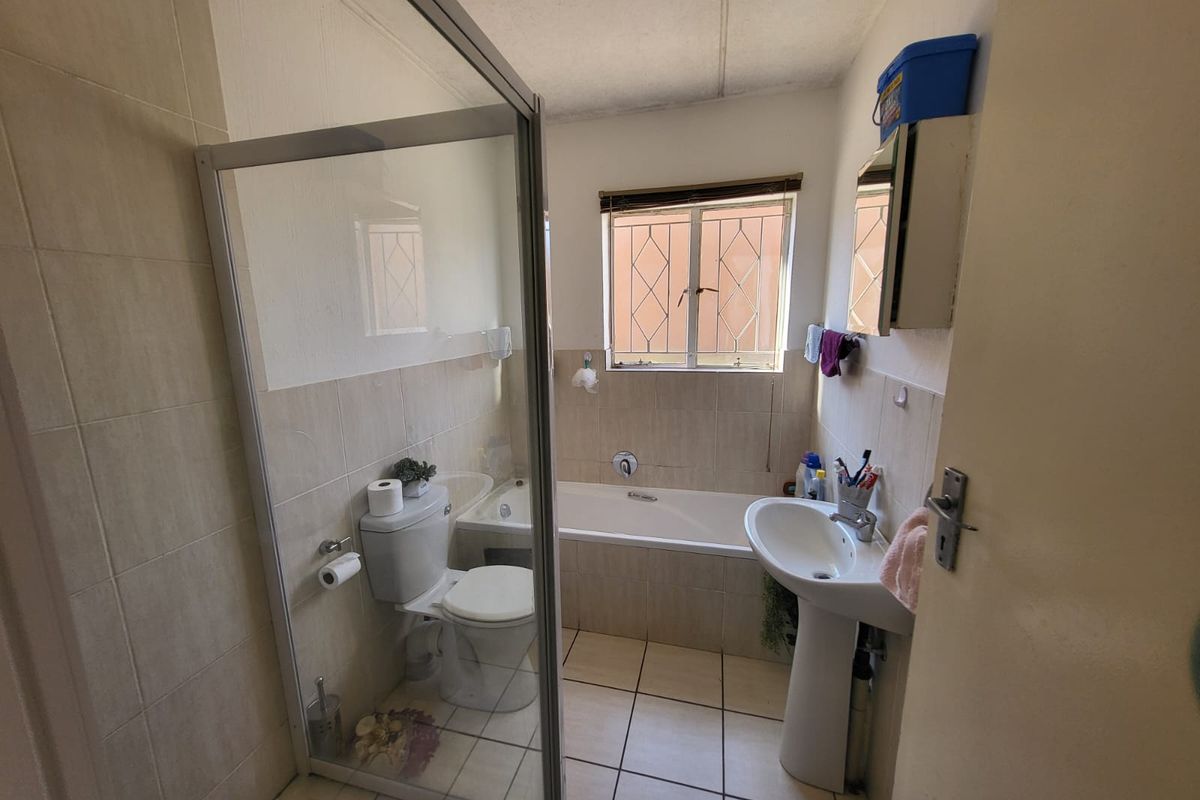 A functional bathroom featuring a shower enclosure, bathtub, pedestal basin, and toilet, with neutral wall and floor tiling.