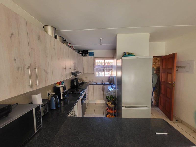 A functional kitchen featuring light wood-look cabinetry, dark laminate countertops, a double basin sink, and tiled flooring with an integrated oven and extractor fan.