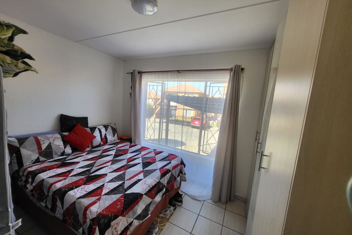A functional bedroom featuring tiled flooring, a built-in wardrobe, and a window fitted with a security gate, providing natural light and ventilation.