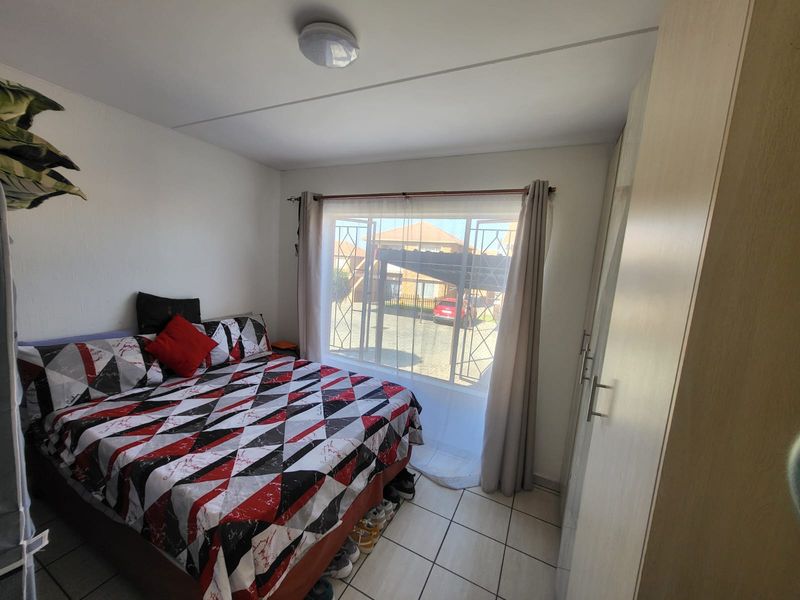 A functional bedroom featuring tiled flooring, a built-in wardrobe, and a window fitted with a security gate, providing natural light and ventilation.