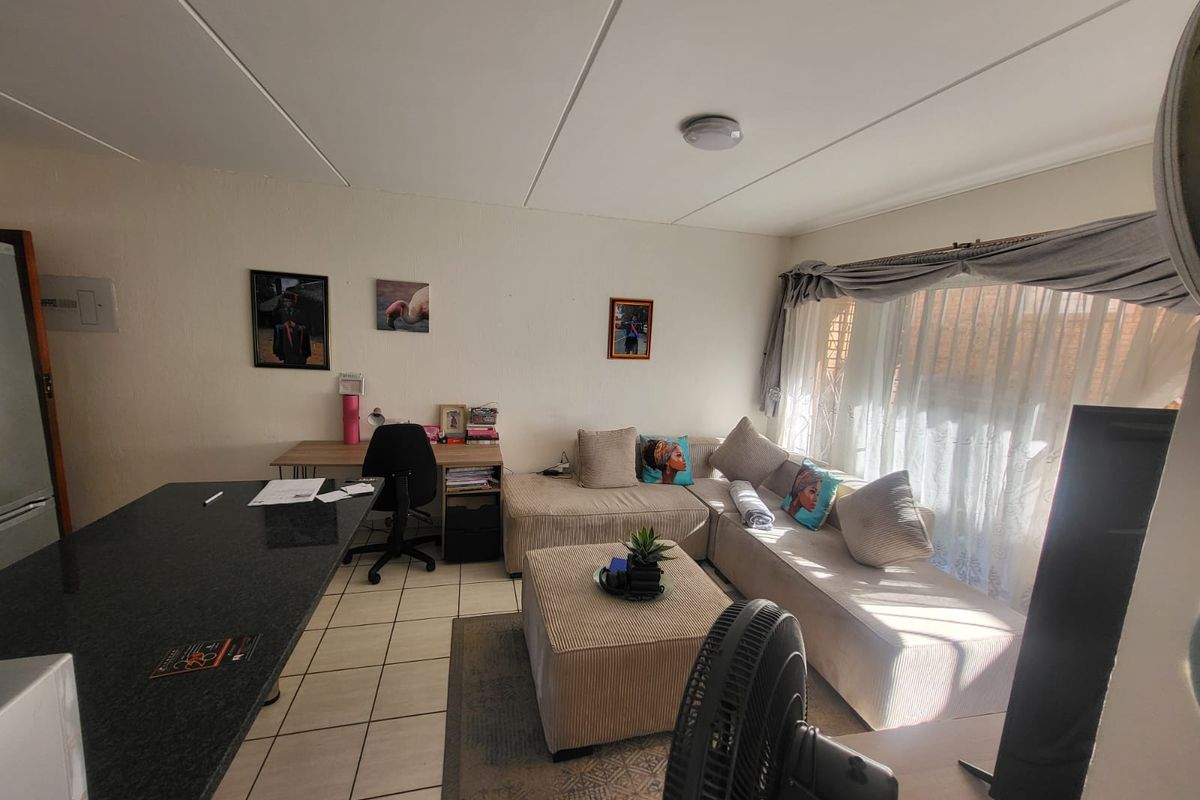 Open-plan living area featuring tiled flooring, a granite breakfast bar, and large windows with curtain tracks, offering a functional and versatile living space.