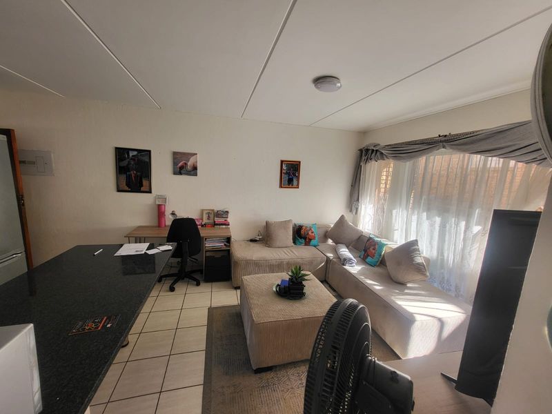 Open-plan living area featuring tiled flooring, a granite breakfast bar, and large windows with curtain tracks, offering a functional and versatile living space.