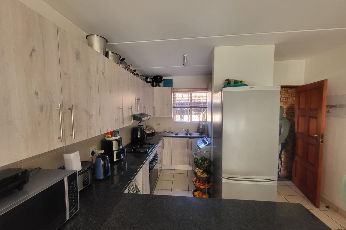 Functional kitchen featuring light wood-look cabinetry, dark granite countertops, built-in oven, hob, and extractor fan with tiled flooring.