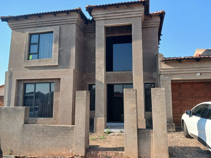 Front elevation of a double-storey house featuring a tiled roof, aluminium window frames, and an attached garage, currently requiring exterior finishing and landscaping.