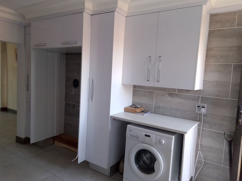 A functional laundry area featuring modern white built-in cabinetry, tiled backsplash, and a dedicated space for a washing machine with a countertop.