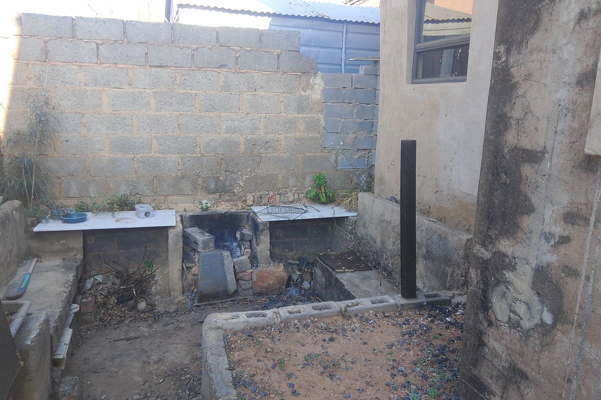 Rear outdoor area featuring a basic built-in braai and concrete block boundary walls, requiring maintenance and cosmetic upgrades.
