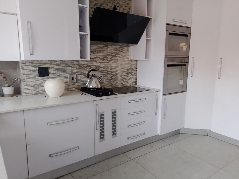 Modern kitchen featuring white cabinetry, quartz countertops, a mosaic tile backsplash, and integrated appliances including a built-in oven and microwave.
