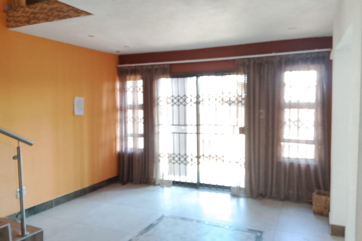 An empty living room featuring tiled floors, a staircase with a metal railing, and a sliding glass door with an integrated security gate.