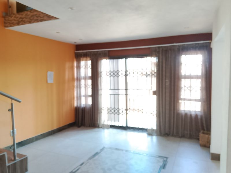 An empty living room featuring tiled floors, a staircase with a metal railing, and a sliding glass door with an integrated security gate.