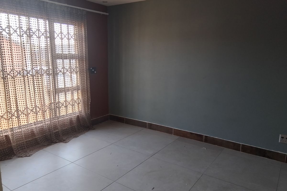 An empty bedroom featuring neutral tiled flooring, recessed downlighting, and a security gate over the window.