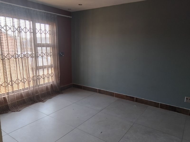 An empty bedroom featuring neutral tiled flooring, recessed downlighting, and a security gate over the window.