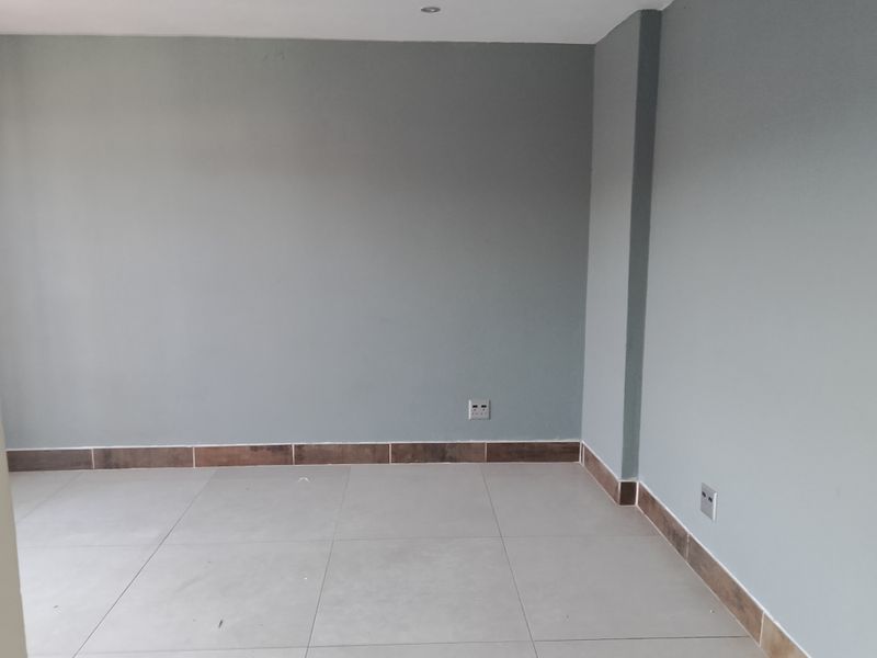 An empty bedroom featuring neutral grey walls, large format floor tiles, and matching tiled skirting boards.