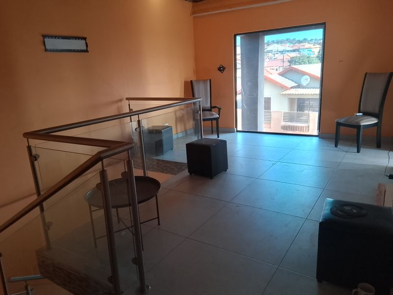 A landing or hallway area featuring tiled flooring, a modern glass balustrade, and a large window providing natural light and neighborhood views.